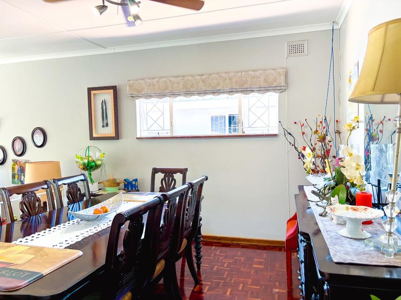 A dining room featuring traditional parquet flooring, a ceiling fan, and a sliding window with a fabric pelmet.