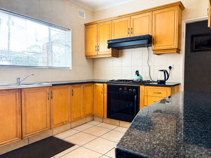 A functional kitchen featuring timber cabinetry, granite countertops, a built-in oven, gas cooktop, and tiled splashback, offering a classic layout with ample storage.