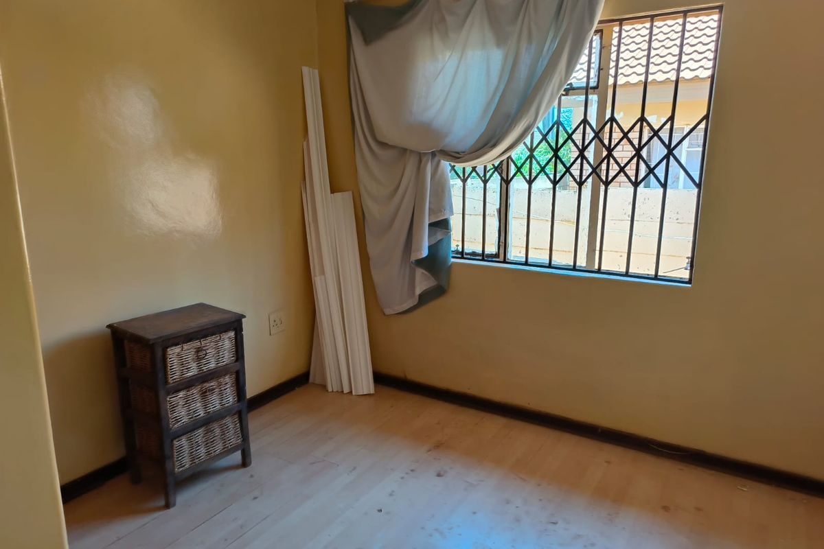A bedroom featuring a window with security bars, light-colored flooring, and neutral wall paint, currently in need of cosmetic updates.