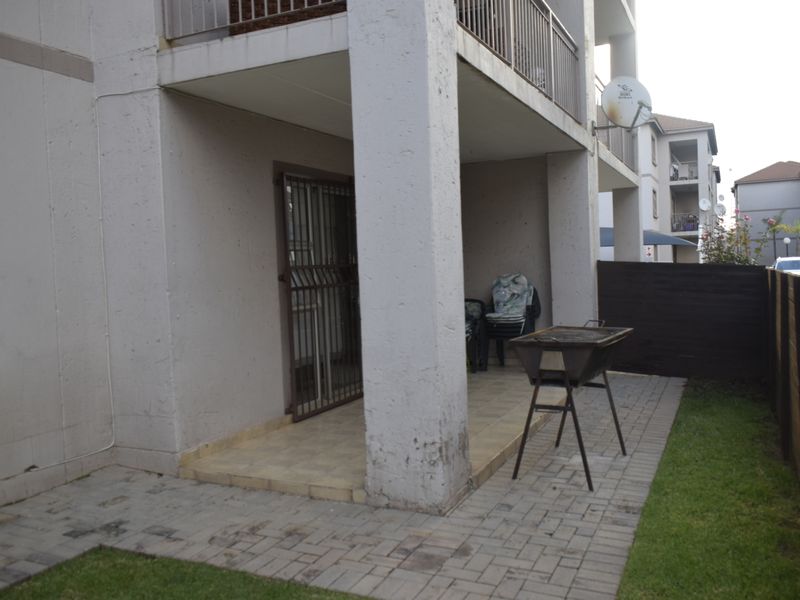 A ground-floor patio area featuring tiled flooring, a security gate, and direct access to a small paved garden space with wooden fencing.