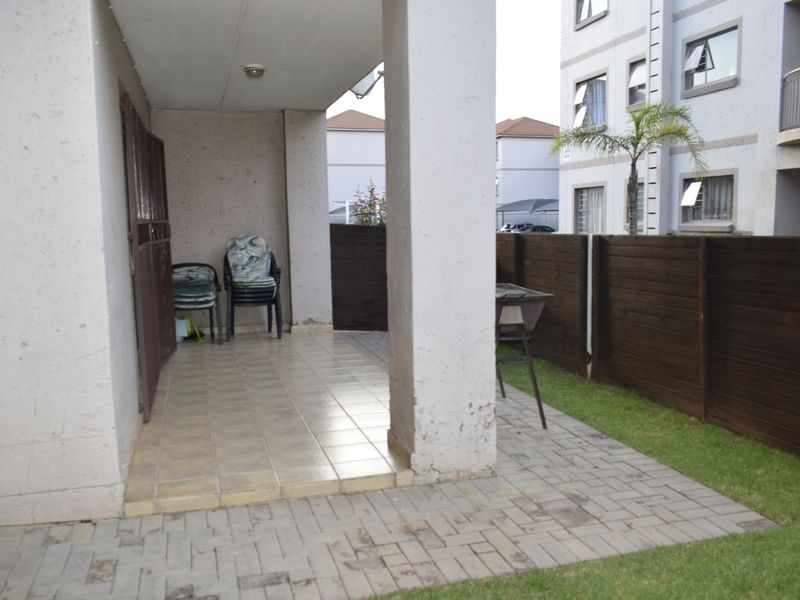 A covered patio area featuring tiled flooring, a concrete support pillar, and an adjacent paved garden space enclosed by a timber fence.