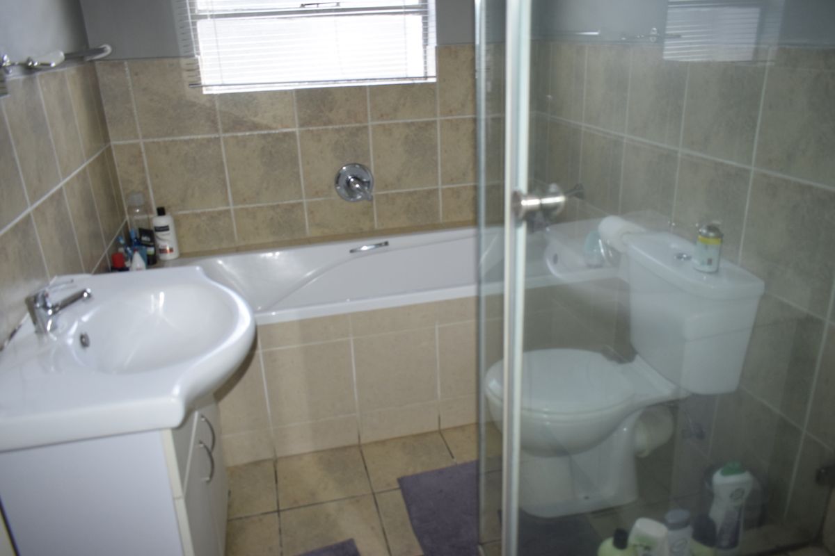 A functional bathroom featuring a built-in bathtub, vanity basin, toilet, and a glass-enclosed shower with neutral wall and floor tiling.