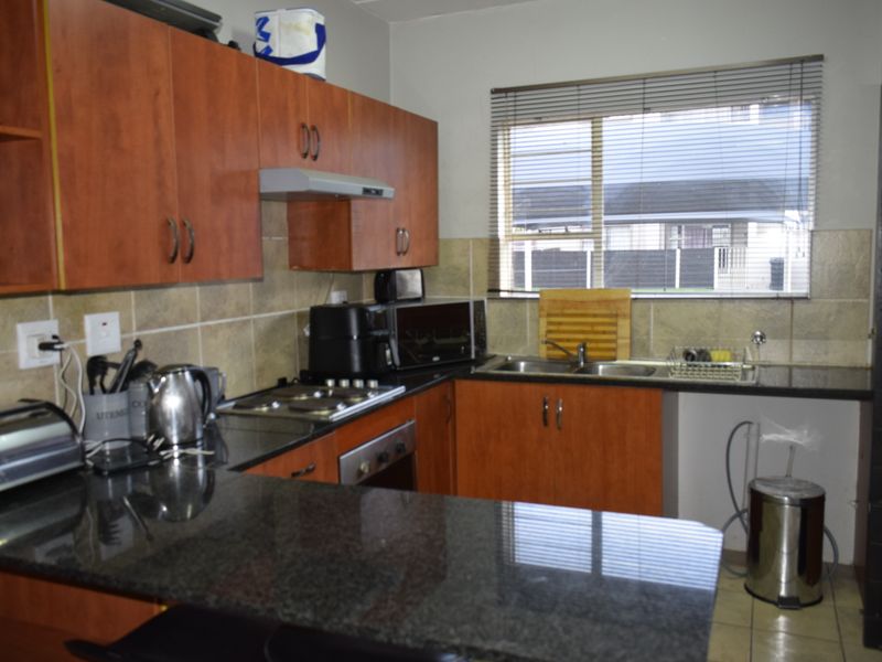 Functional kitchen featuring granite countertops, built-in oven, electric hob, extractor fan, and ample cabinetry with a tiled backsplash and window view.
