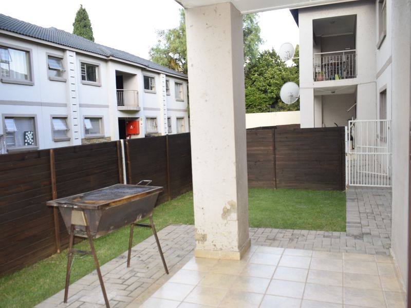A covered patio area featuring tiled flooring and a concrete support pillar, leading out to a small private garden with timber fencing.