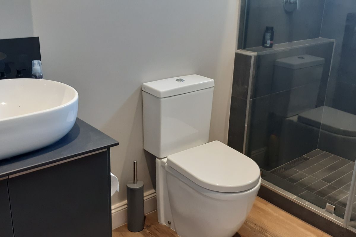 Modern bathroom featuring a sleek vanity with vessel sink, a contemporary toilet, and a walk-in shower with dark tiled finishes.