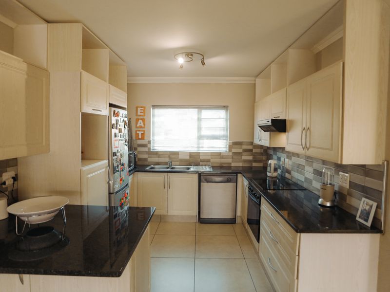 A functional kitchen featuring light-toned cabinetry, dark granite countertops, a tiled backsplash, and integrated appliances, offering a practical layout for daily cooking.