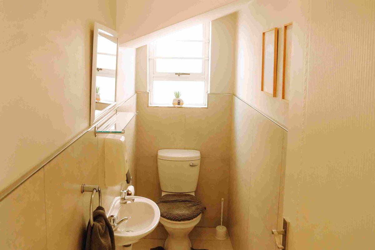 A compact guest bathroom featuring a pedestal basin, toilet, and neutral wall tiling with a small louvre window for ventilation.