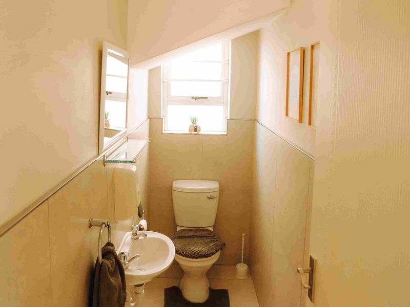 A compact guest bathroom featuring a pedestal basin, toilet, and neutral wall tiling with a small louvre window for ventilation.