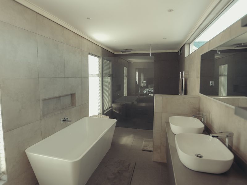 Modern, spacious bathroom featuring a freestanding bathtub, double vessel sink vanity, and a large walk-in shower with contemporary neutral tiling.
