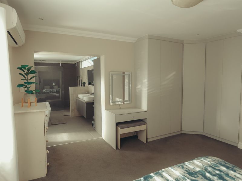 Spacious bedroom featuring extensive built-in cupboards, an integrated vanity area, and direct access to a modern en-suite bathroom with dual vanity.