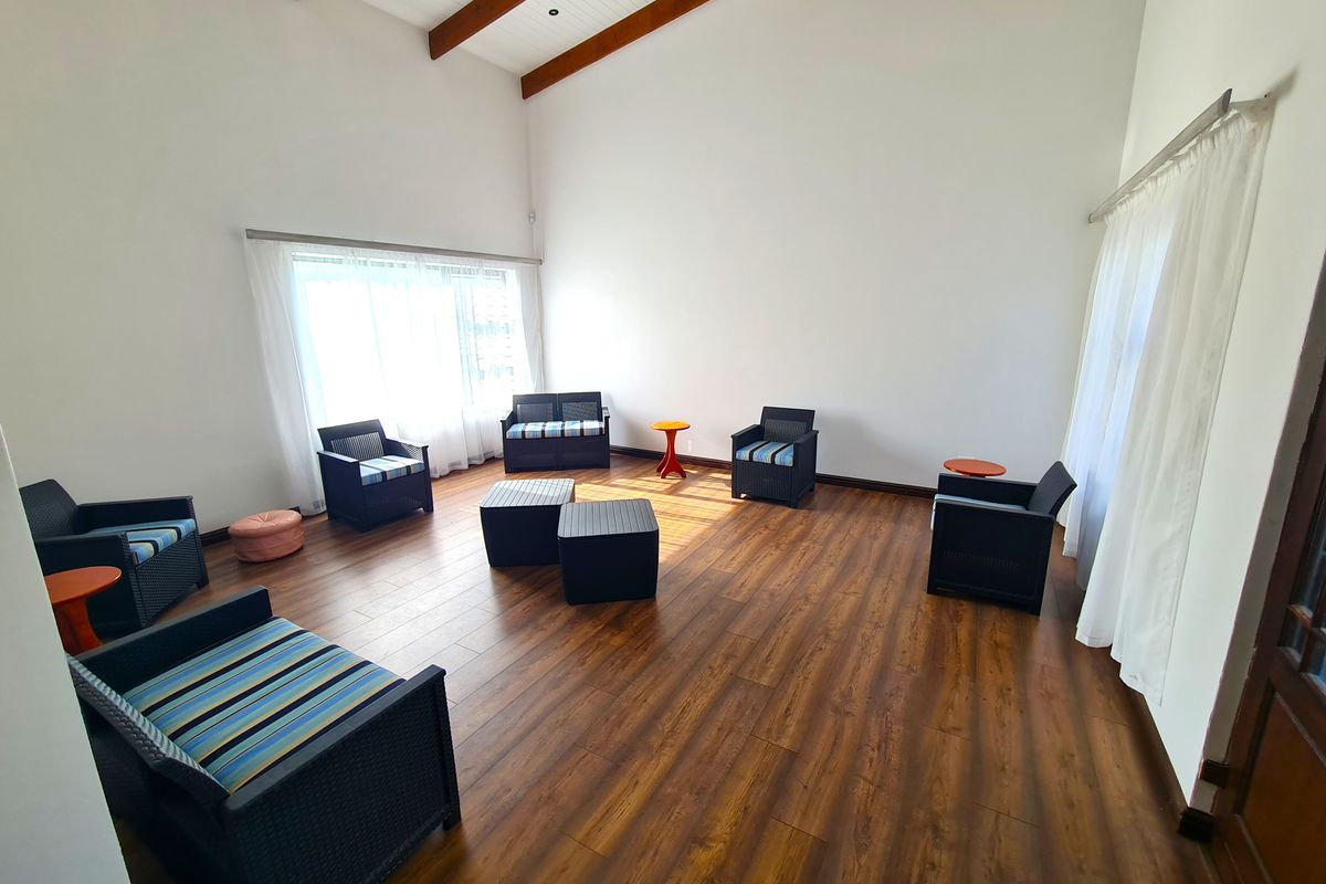 Spacious living room featuring high vaulted ceilings with exposed timber beams and warm-toned laminate wood flooring, illuminated by large windows.