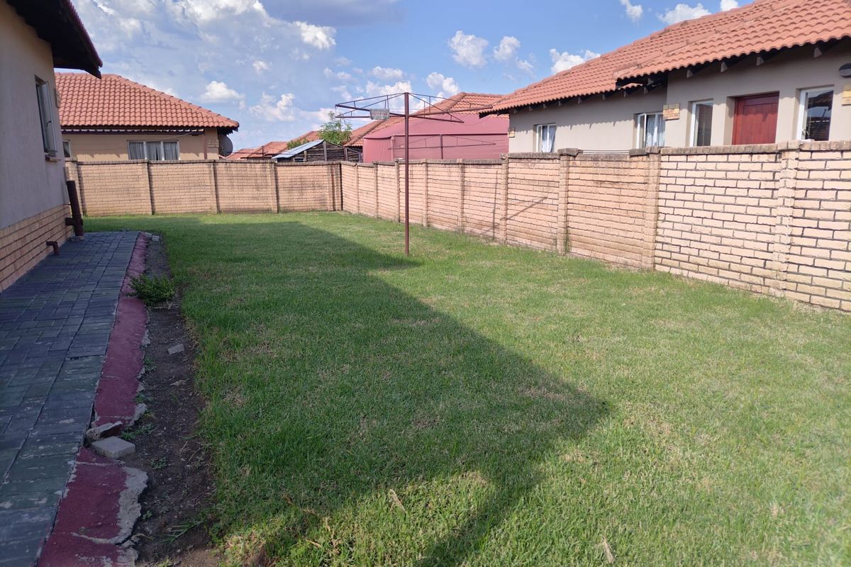 A private rear garden featuring a lawn, paved walkway, and secure brick boundary walls, providing a functional outdoor space.
