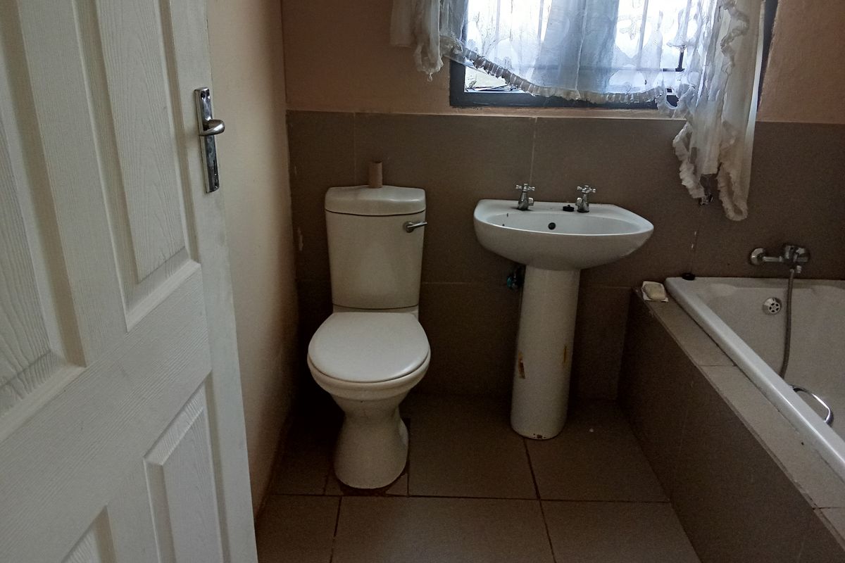 A dated bathroom featuring a standard toilet, pedestal sink, and a built-in bathtub with tiled surround.