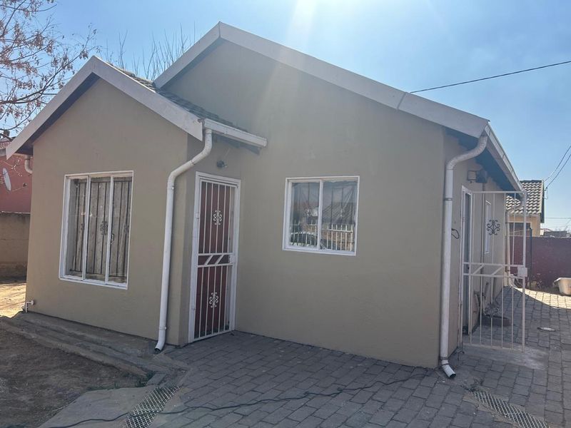 A single-story residential house featuring a neutral exterior finish, security gates, and paved outdoor area, presenting a functional and well-defined building structure.