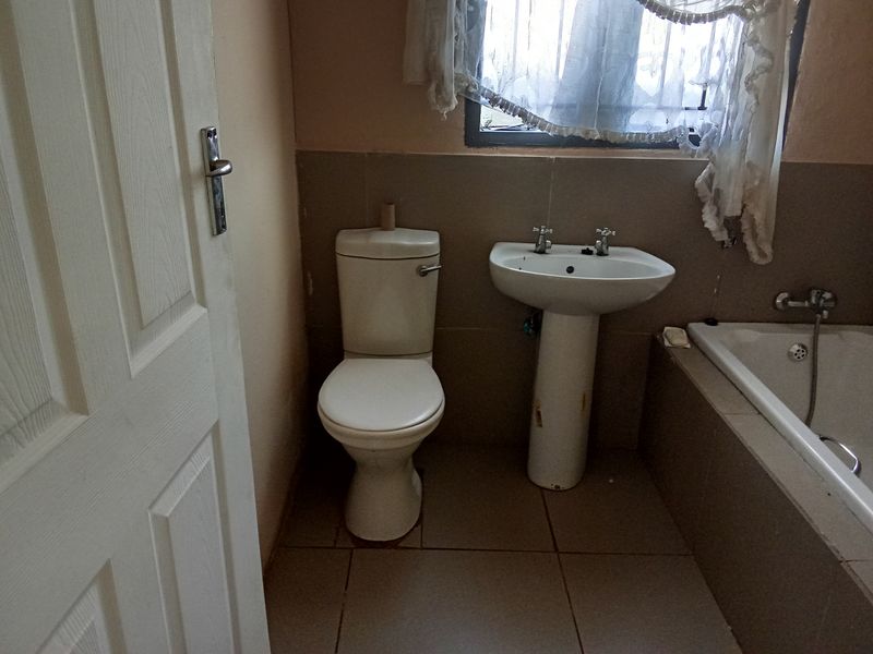 A dated bathroom featuring a standard toilet, pedestal sink, and a built-in bathtub with tiled surround.