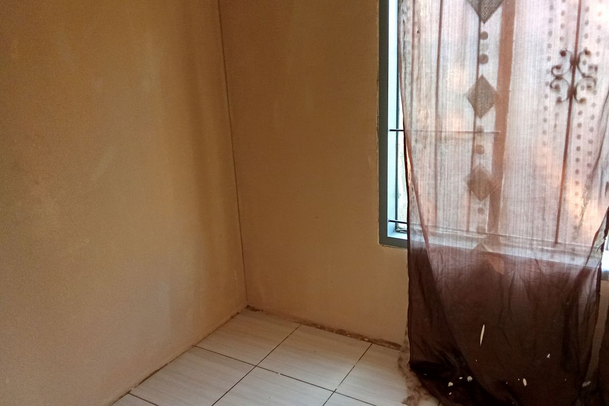 A simple bedroom featuring tiled flooring and a window with security bars, offering a blank canvas for potential interior updates.