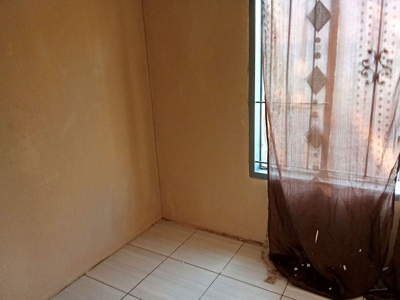 A simple bedroom featuring tiled flooring and a window with security bars, offering a blank canvas for potential interior updates.