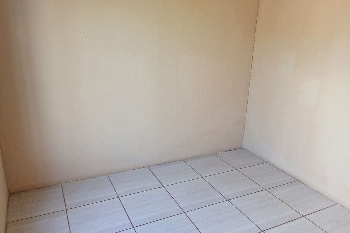 A simple, empty room featuring neutral wall paint and light-colored ceramic floor tiles, providing a blank canvas for potential interior design.