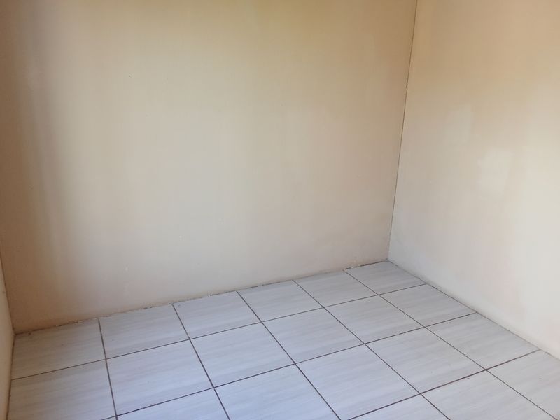A simple, empty room featuring neutral wall paint and light-colored ceramic floor tiles, providing a blank canvas for potential interior design.