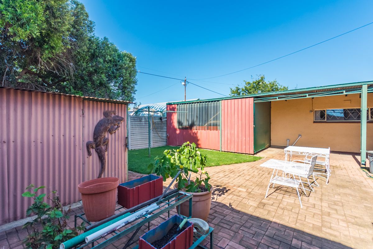 A paved rear courtyard area featuring corrugated metal outbuildings, a small lawn section, and a covered patio space.