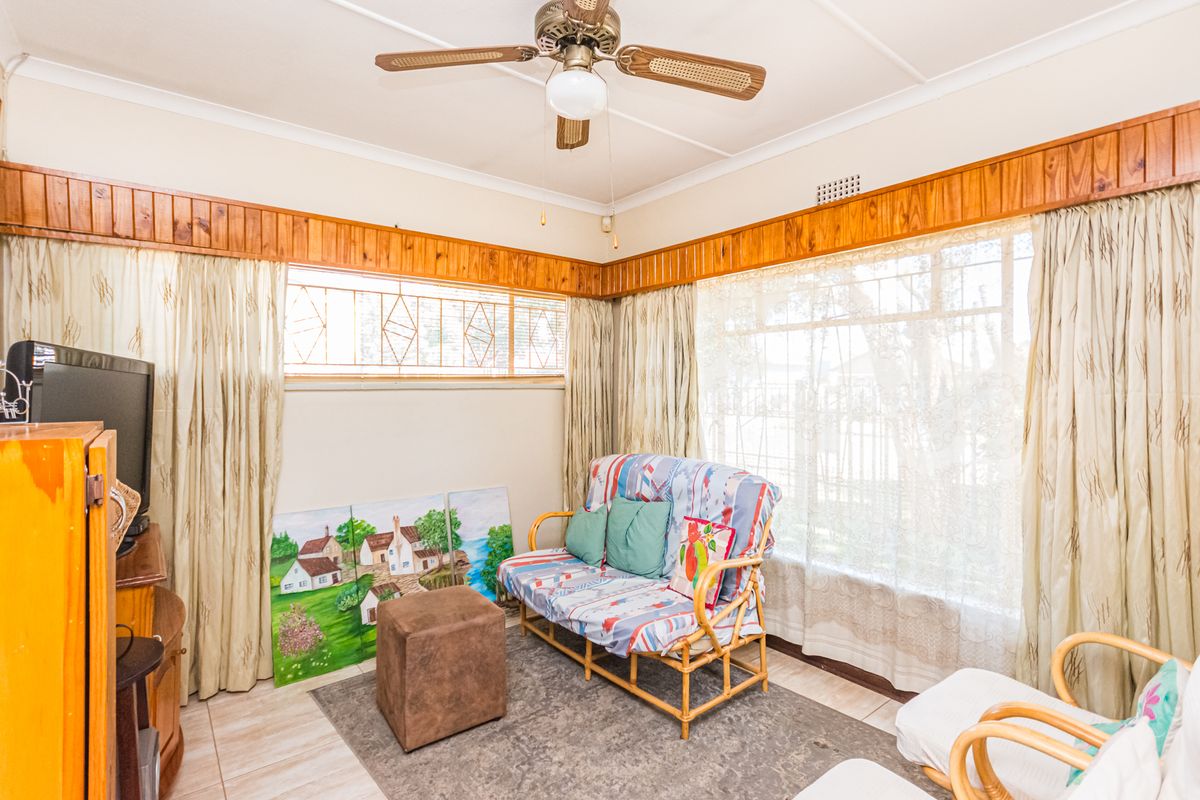 A living room featuring large windows, tiled flooring, and a ceiling fan, characterized by traditional timber wall accents.