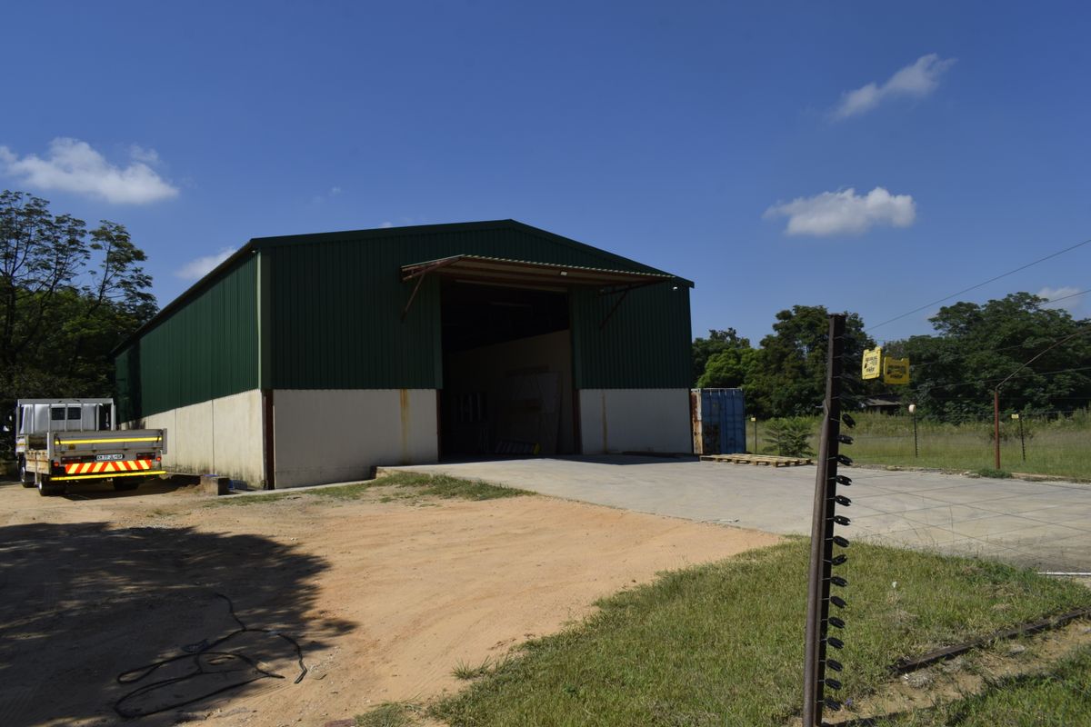 Large industrial-style utility shed with corrugated metal siding, concrete apron, and perimeter electric fencing on a farm property.