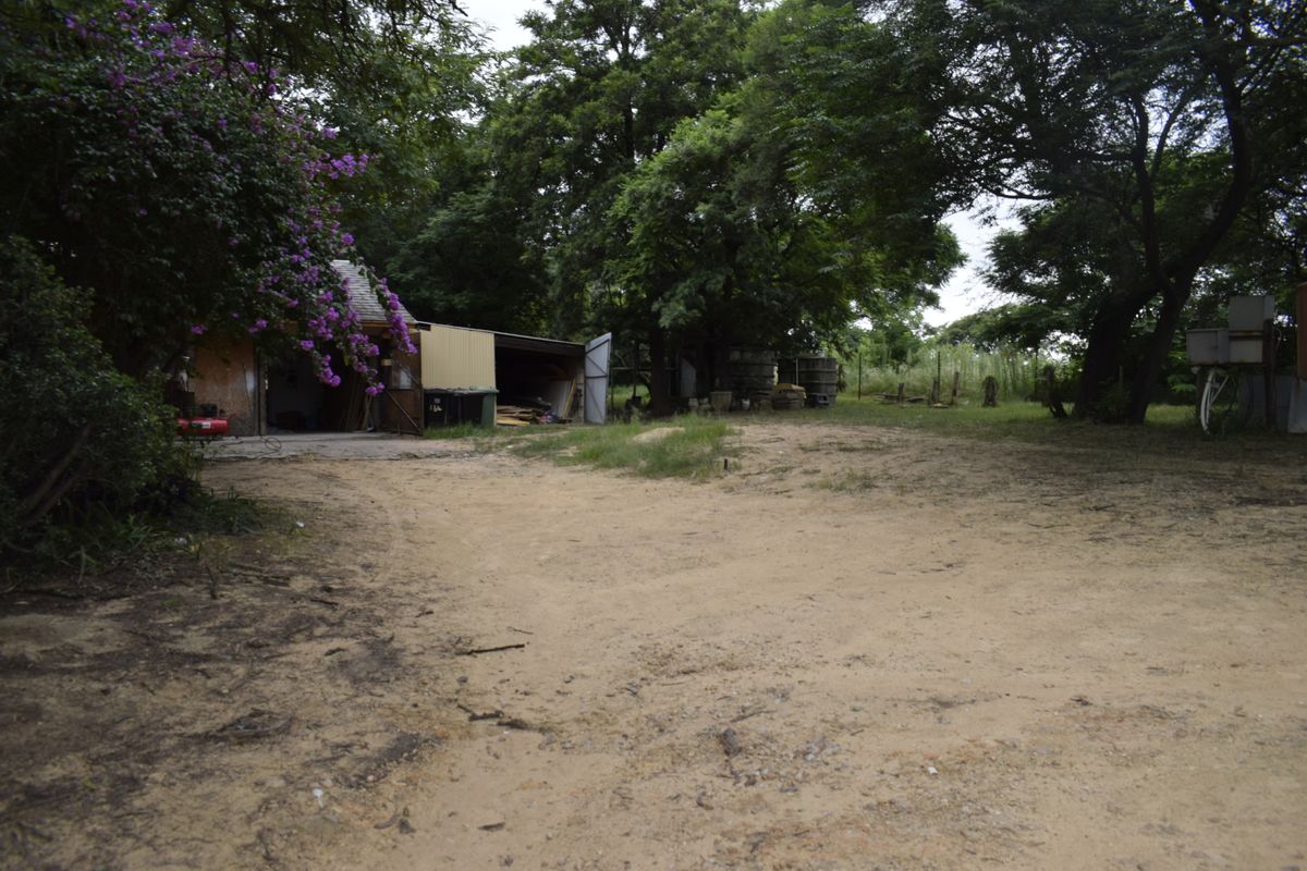 A view of the rear farm yard featuring an outbuilding, unpaved ground, and mature trees.