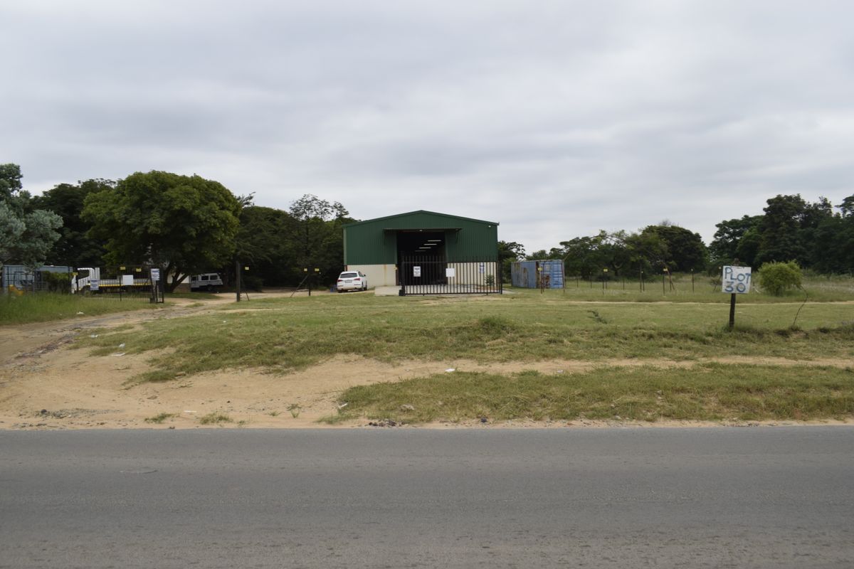Front view of a farm property featuring a large metal shed, gated entrance, and open land area accessible from the road.