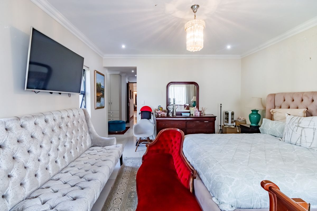 Spacious bedroom featuring crown molding, recessed lighting, a crystal chandelier, and tiled flooring, with an adjoining hallway visible.