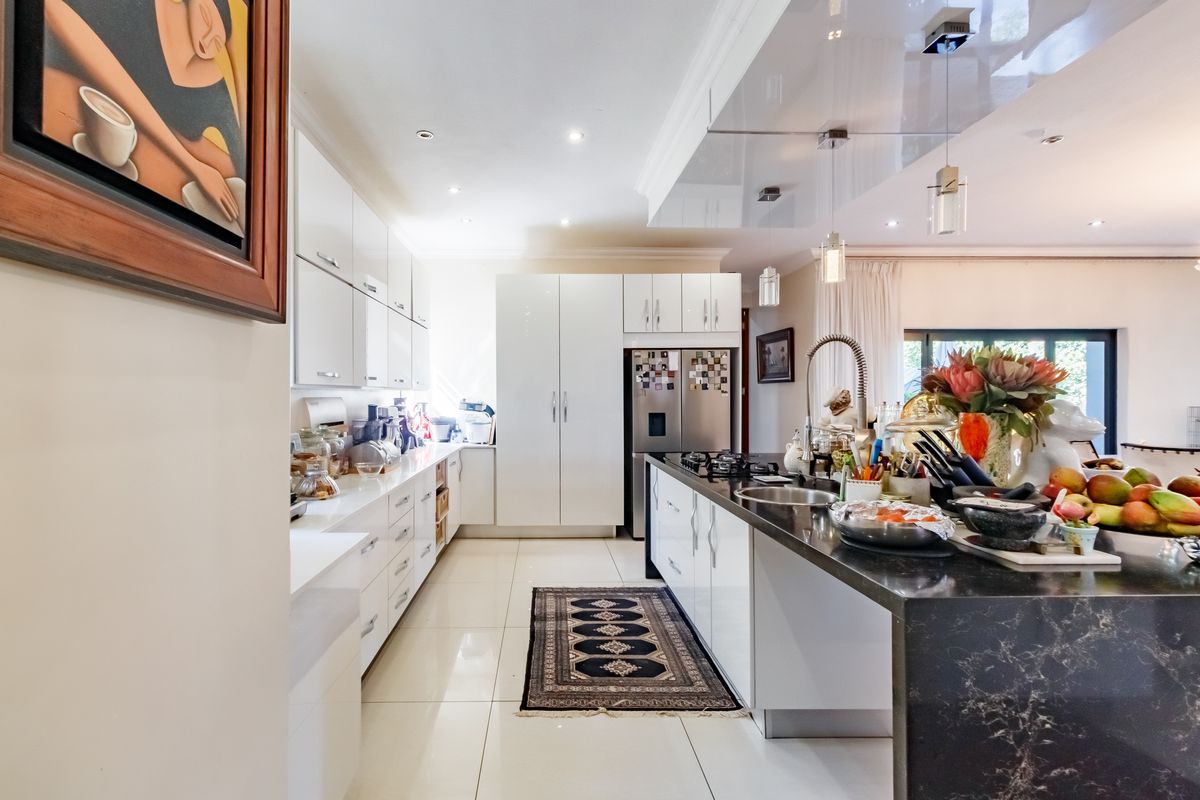 Modern kitchen featuring high-gloss white cabinetry, a large black stone island with integrated gas hob, and sleek tiled flooring.