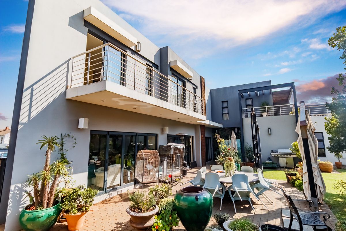 Spacious rear patio area featuring paved flooring, a large balcony above, and modern sliding glass doors leading into the home.