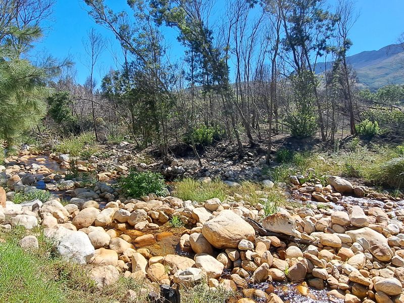A scenic view of a natural rocky stream bed flowing through a rural landscape with mountain vistas in the background.