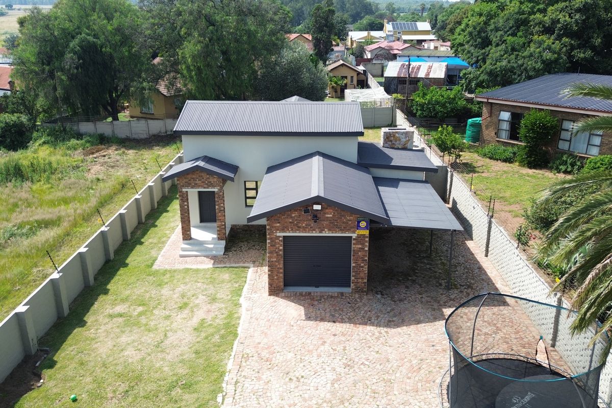 Aerial view of a modern residential property featuring a brick facade, corrugated metal roof, single garage, carport, and a paved driveway.