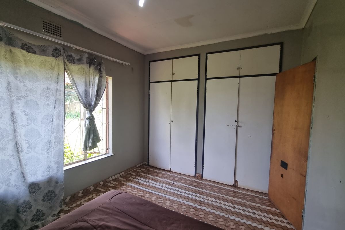 A bedroom featuring built-in cupboards, security bars on the window, and tiled flooring. The room requires cosmetic updates to improve its overall condition.