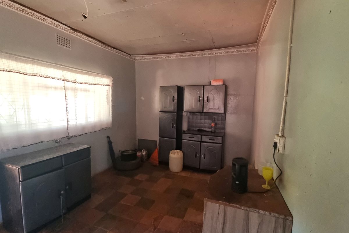 A dated kitchen space featuring original built-in cabinetry, tiled flooring, and decorative ceiling cornices, requiring modernization and cosmetic updates.