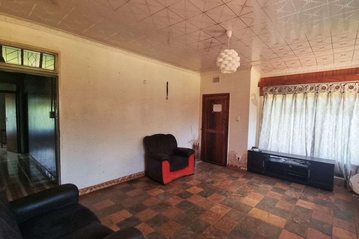 A living room featuring patterned ceiling tiles, tiled flooring, and a wooden door, requiring cosmetic updates to the wall finishes.