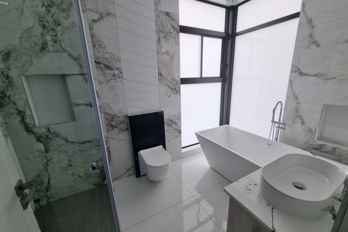 Modern bathroom featuring a freestanding bathtub, wall-mounted toilet, vessel sink, and elegant marble-look wall tiles with large windows for natural light.