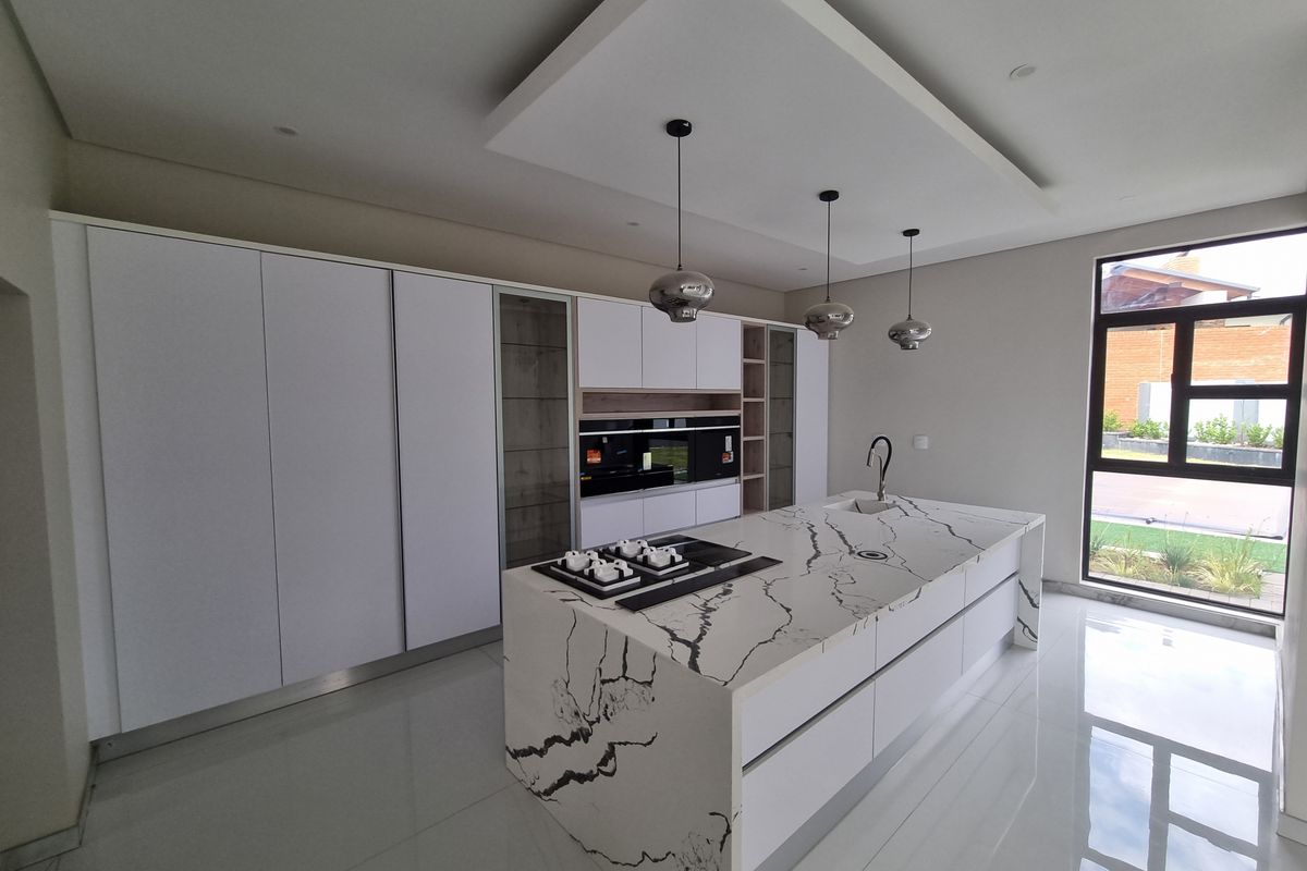 Modern kitchen featuring a large marble-look stone island, integrated appliances, floor-to-ceiling cabinetry, and elegant pendant lighting in a bright, open space.