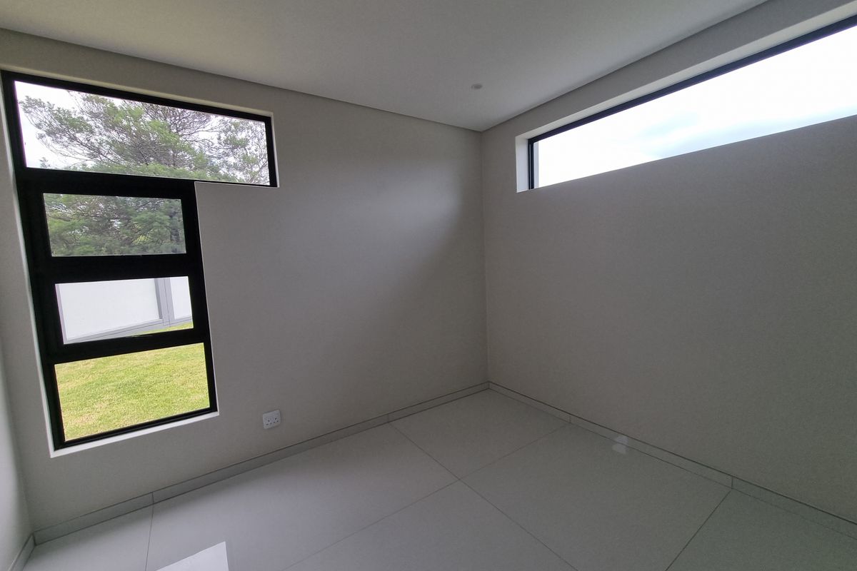 A bright, empty bedroom featuring modern tiled flooring, neutral walls, and large aluminium-framed windows providing natural light.
