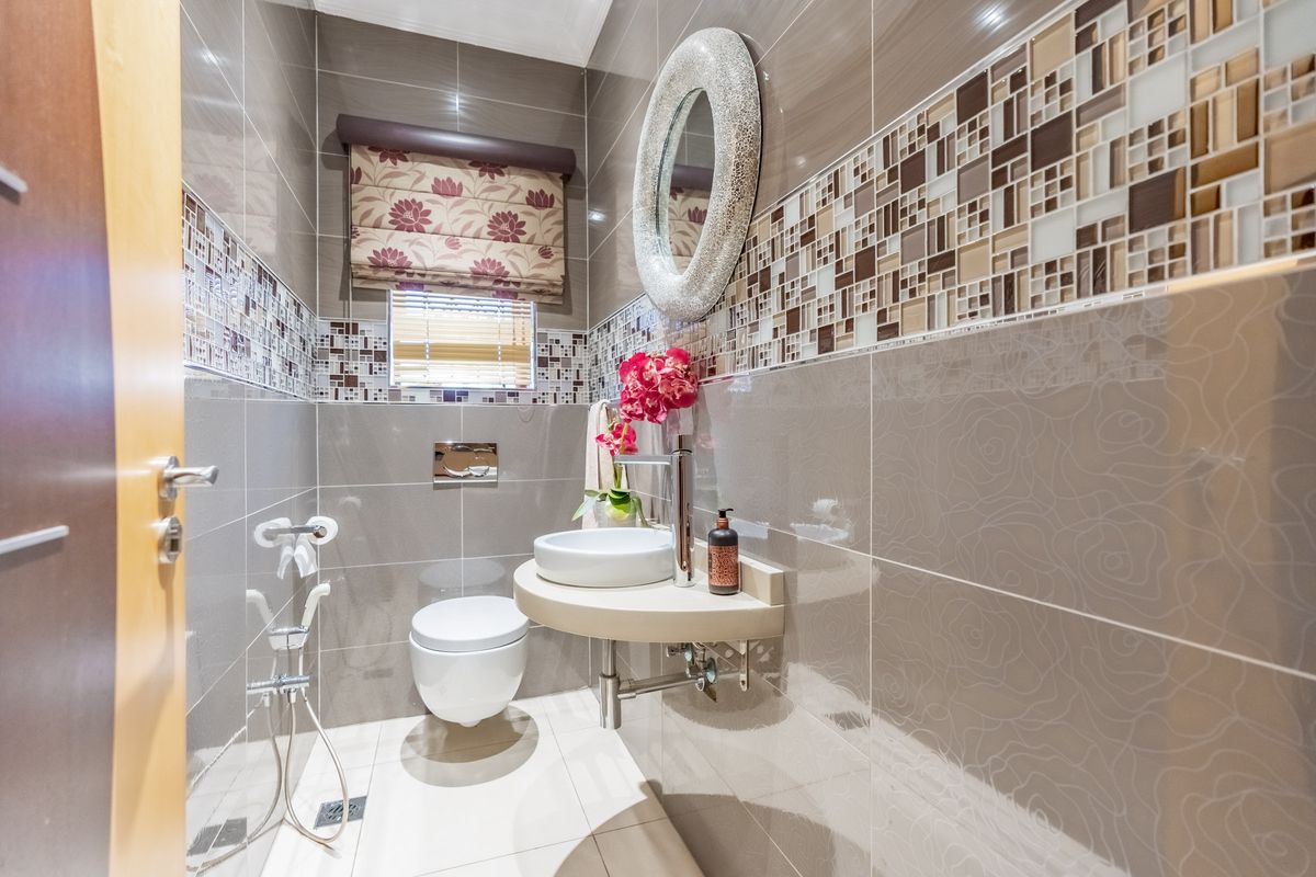 A modern guest bathroom featuring a wall-mounted toilet, vessel sink, and decorative mosaic tile accents with neutral ceramic wall and floor tiles.