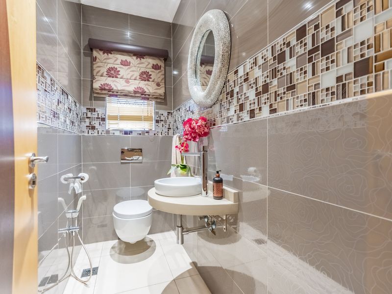 A modern guest bathroom featuring a wall-mounted toilet, vessel sink, and decorative mosaic tile accents with neutral ceramic wall and floor tiles.