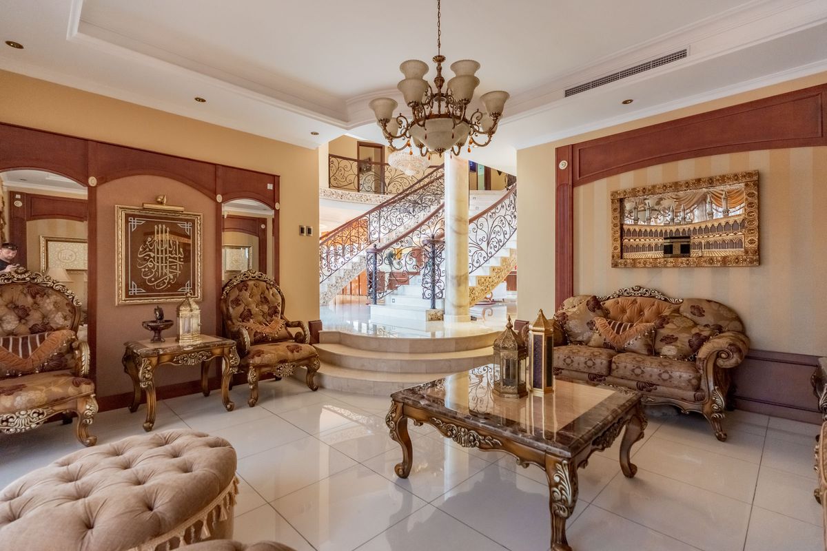 Elegant living room featuring polished marble flooring, a grand wrought iron staircase, and sophisticated decorative wall paneling with integrated lighting.