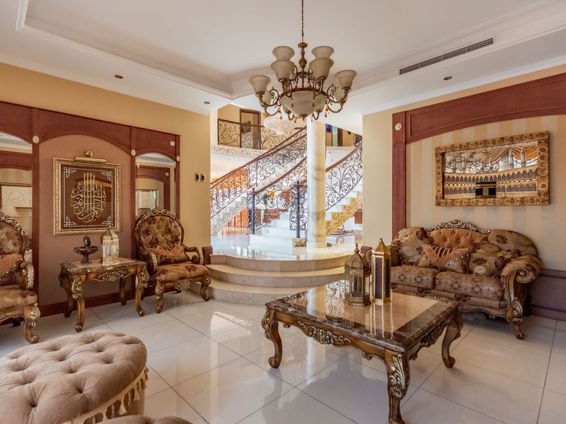 Elegant living room featuring polished marble flooring, a grand wrought iron staircase, and sophisticated decorative wall paneling with integrated lighting.