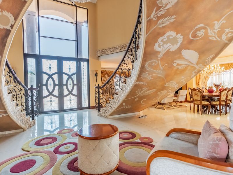 Grand entrance foyer featuring a striking curved staircase with wrought iron balustrades, high ceilings, and large windows providing abundant natural light.
