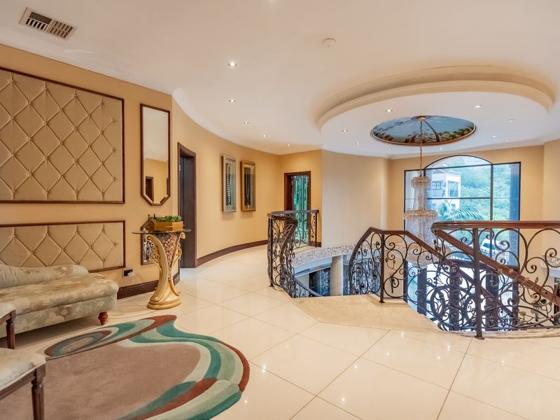 Spacious upper-level landing featuring elegant wrought iron balustrades, polished tile flooring, and a decorative coffered ceiling with recessed lighting.
