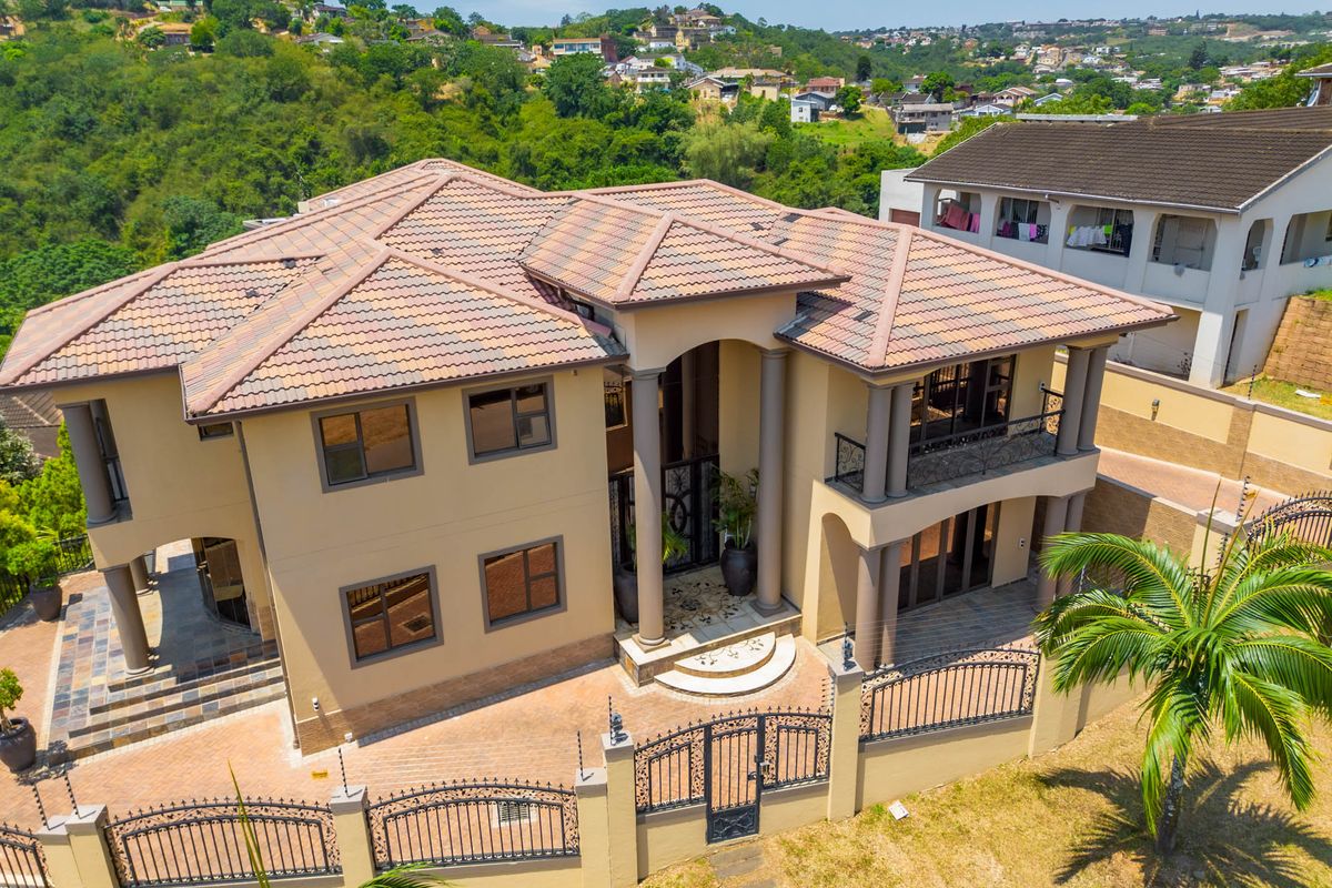 Aerial view of a multi-story residential property featuring a tiled roof, balcony, paved driveway, and secure perimeter fencing.
