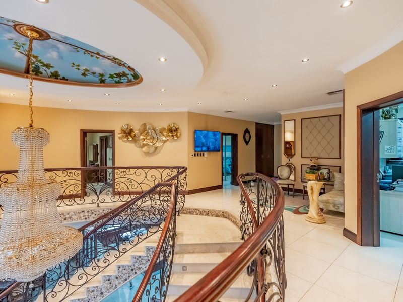 Spacious upper-level landing featuring a grand wrought iron staircase, ornate crystal chandelier, and decorative ceiling detailing with polished tile flooring.