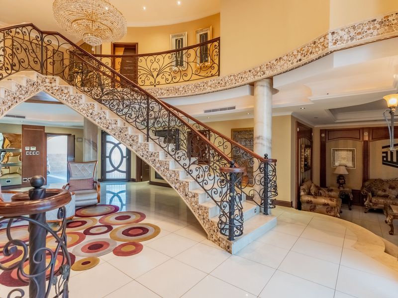 Grand entrance foyer featuring a sweeping staircase with intricate wrought iron railings, marble flooring, and elegant decorative mosaic detailing.