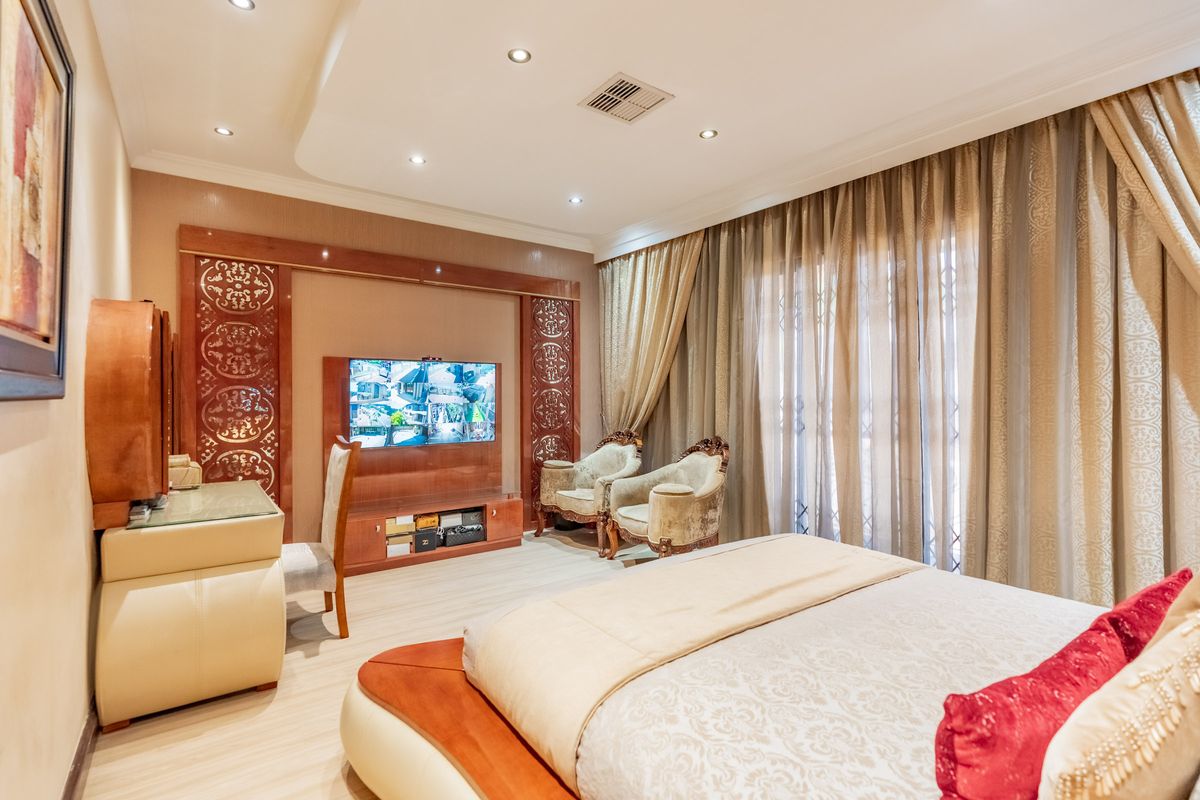 Spacious bedroom featuring a recessed ceiling with downlights, custom built-in media cabinetry, and decorative wall paneling with integrated air conditioning.