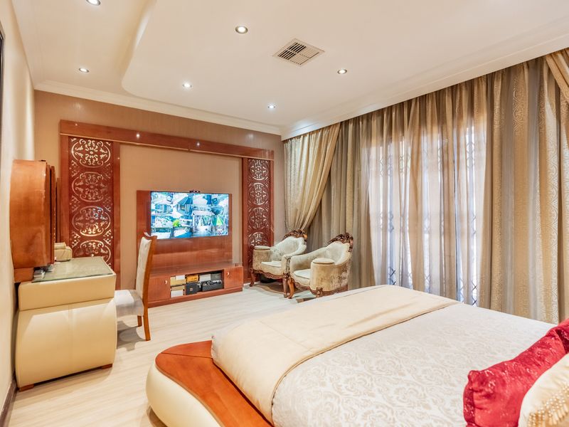 Spacious bedroom featuring a recessed ceiling with downlights, custom built-in media cabinetry, and decorative wall paneling with integrated air conditioning.